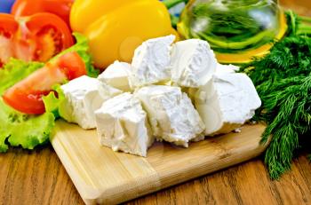Slices of feta cheese, tomatoes, yellow sweet peppers, lettuce, a bottle of oil, dill on wooden board