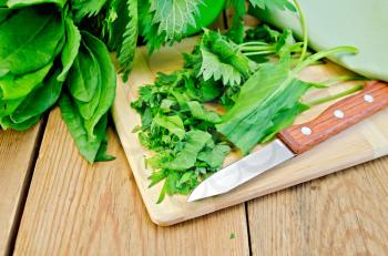 Fresh chopped sorrel and nettles on a plate with a knife on a wooden boards background
