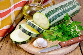 Green striped zucchini, garlic, a bottle of vegetable oil, parsley, napkin, knife on a wooden board