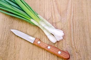 Bunch of fresh green onions with a knife on a wooden boards background