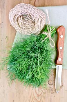 Fresh dill green with a ball of twine and a knife on a napkin on the background of wooden boards