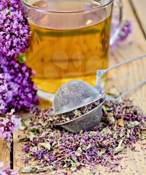 Herbal tea in glass mug, metal sieve with dry flowers marjoram, fresh flowers of oregano on the background of wooden boards