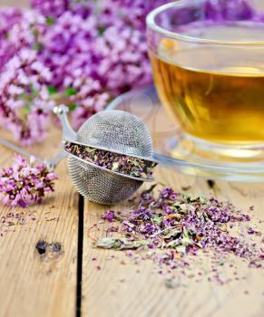 Metal sieve with dried flowers of oregano, a herbal tea in a glass cup, fresh flowers of oregano on the background of wooden boards