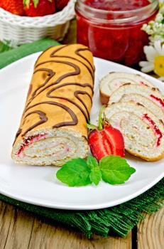 Biscuit roulade with cream and jam, jar of jam, doily, strawberries, mint on the background of wooden boards