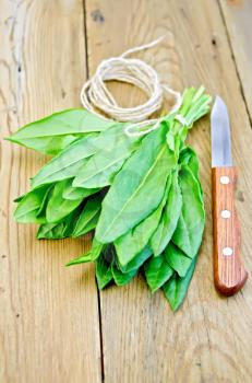 Bunch of green sorrel with knife and twine on the background of wooden boards