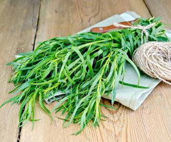 Tarragon fresh green with a ball of twine and a knife on a napkin on the background of wooden boards
