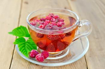 Tea with raspberries in a glass cup, green raspberry leaf on the background of wooden boards