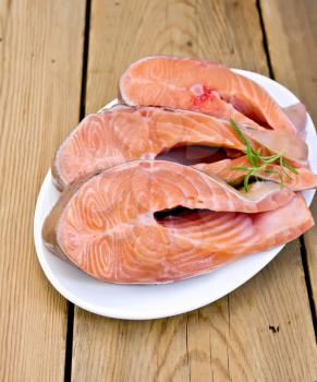 Three pieces of trout in white plate with rosemary on a wooden boards background