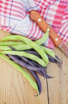 Asparagus beans green and purple, napkin, knife on background wooden plank