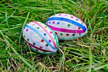 Two easter eggs, decorated with multicolored braid and sparkles as asterisks on the green grass