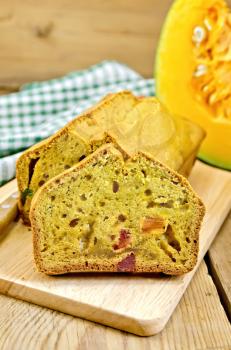 Pumpkin cake with candied fruit on the board, pumpkin, knife, napkin on the background of wooden boards
