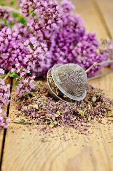 Flowers fresh and dry oregano in a metal strainer on a wooden boards background