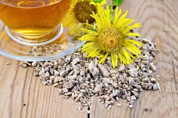 Elecampane root, fresh yellow flower elecampane, tea in a glass cup on a wooden boards background