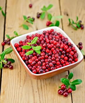 Ripe red lingonberries in a bowl with a sprig of berries and leaves on the background of wooden boards
