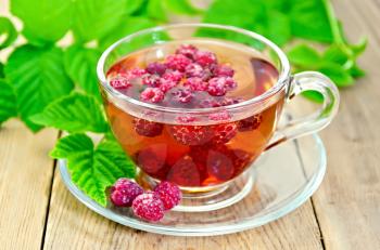 Tea with raspberries in a glass cup, green raspberry leaves on the background of wooden boards