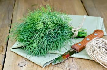 Sheaf of dill, ball of twine, a knife and a napkin on the background of wooden boards