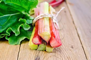 Bundle of stalks rhubarb, tied with twine, rhubarb leaves on the background of wooden boards