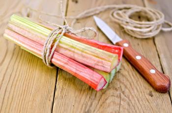 Bundle of stalks of rhubarb, a knife and a coil of rope on the background of wooden boards