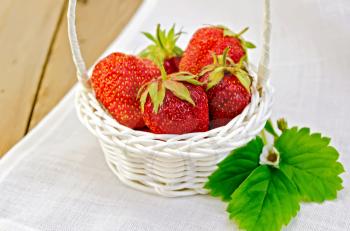 Ripe red strawberries in a white wicker basket on a napkin on the background of wooden boards