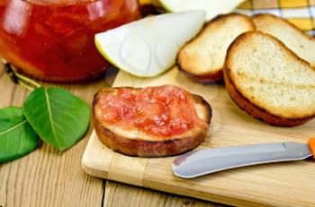 Slices of toasted bread, a glass jar with pear jam, knife on background wooden board