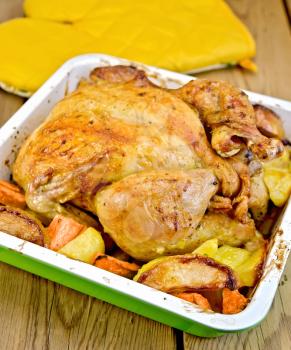Chicken baked with potatoes, carrots and apples in a tray, potholder on the background of wooden boards