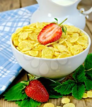 Cornflakes in a white bowl, leaves and strawberries, milk in a jug, a napkin on the background of wooden boards