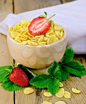 Cornflakes in wooden bowl, strawberry leaves and berries, a napkin on a wooden boards background