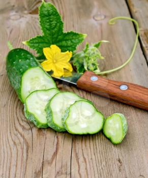 Sliced cucumber with yellow flower and green leaf, knife on a wooden board