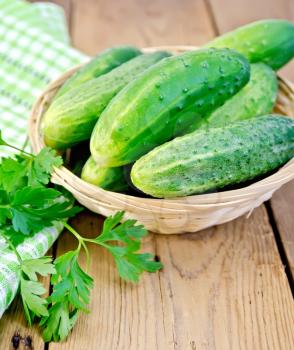 Cucumbers in a wicker basket, parsley, doily on a wooden boards background