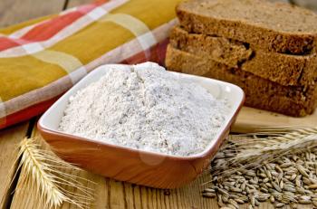 Rye flour in a bowl, homemade loaves of rye bread, spikelets and grain of rye, napkin on wooden board