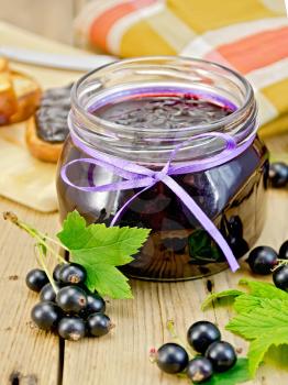 Black currant jam in a glass jar, fresh blackcurrant with leaves, napkin on a wooden board