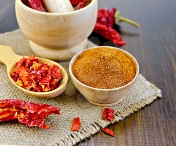 Red pepper powder in a wooden bowl of dry cereal and pods of red pepper in a mortar and a wooden spoon, sacking on a wooden board
