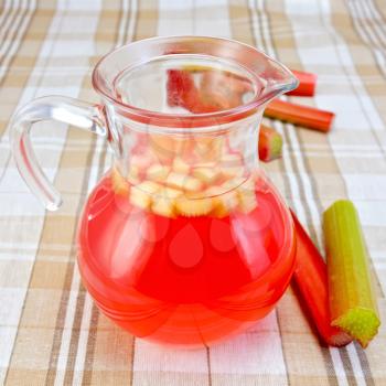 Compote from rhubarb in a glass jug, rhubarb stalks on tablecloth background