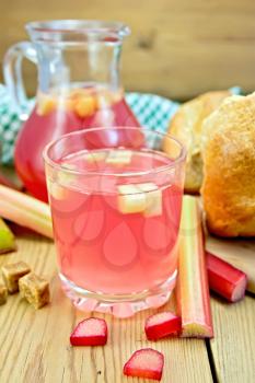 Compote from rhubarb in a glass and pitcher, sugar, bread, rhubarb stalks, doily on a wooden boards background
