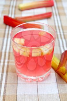 Compote from rhubarb in a glass, rhubarb stalks on tablecloth background