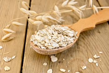 Oat flakes in wooden spoon, stalks of oats on the background of wooden boards