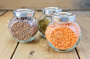 Lentils red, green, brown in glass jars on a wooden boards background