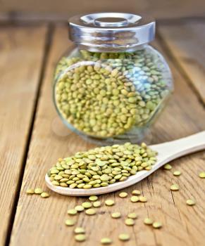 Green lentils in a glass jar and a wooden spoon on a wooden boards background