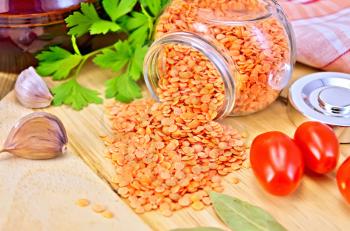 Red lentils in a glass jar, parsley, garlic, tomatoes, clay pot, napkin on wooden board