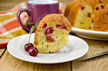 Cherry cake on a plate with cherry berries, napkin, knife, mug on the background of wooden boards
