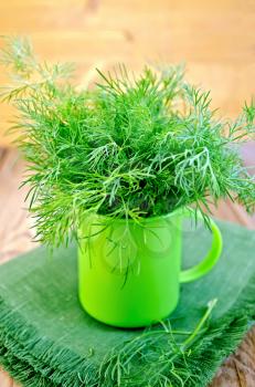 Fresh green dill in a plastic mug, napkin on the background of wooden boards