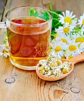 Wooden spoon with dried chamomile flowers, a bouquet of fresh flowers of chamomile tea in glass mug on the background of wooden boards