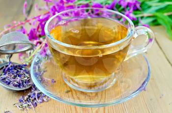 Herbal tea in a glass cup, metal sieve with dry flowers fireweed, fireweed fresh flowers on a wooden board