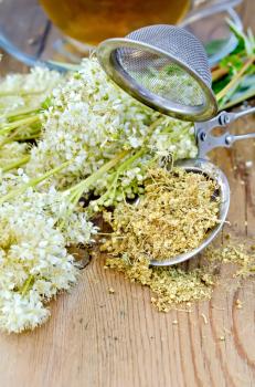 Metal sieve with dried flowers of meadowsweet, a bouquet of fresh flowers of meadowsweet, tea in a glass cup on a wooden board