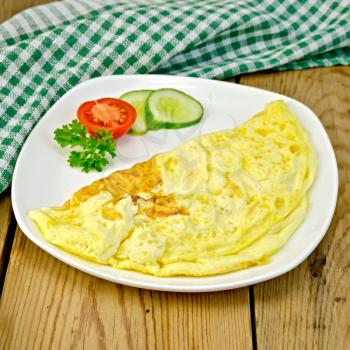 Omelette with slices of tomato, cucumber and parsley on a plate, napkin on the background of wooden boards