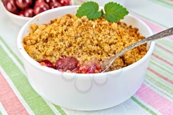 Cherry crumble in a white bowl with a spoon, cherries on a background of striped linen tablecloth