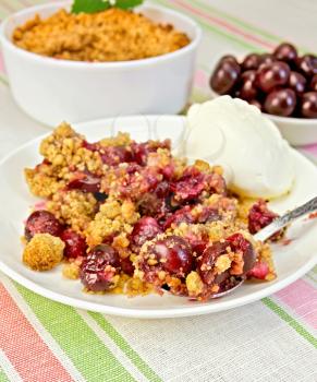 Cherry crumble in a white bowl and a plate with a spoon, cherries on a background of striped linen tablecloth