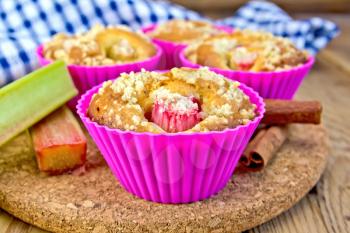 Cupcakes in tins with rhubarb, rhubarb, cinnamon, napkin on the background of wooden boards