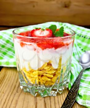 Milk dessert with strawberries, corn flakes and yogurt, spoon, napkin on the background of wooden boards