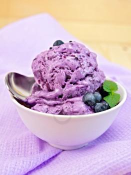Blueberry ice cream with mint leaves in a bowl with berries, mint and spoon on a background of purple cloth and wooden boards